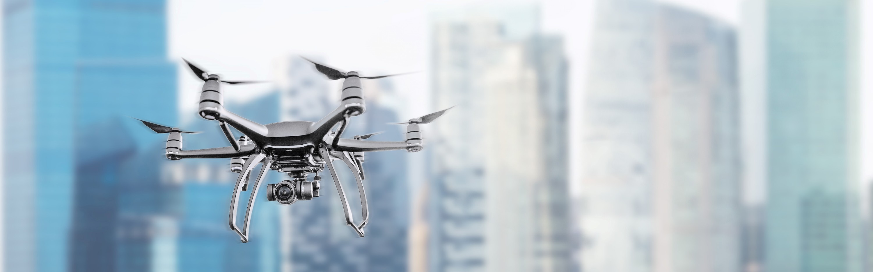 : Mehrrotor-Drohne mit Kamera fliegt vor einer urbanen Hochhauskulisse